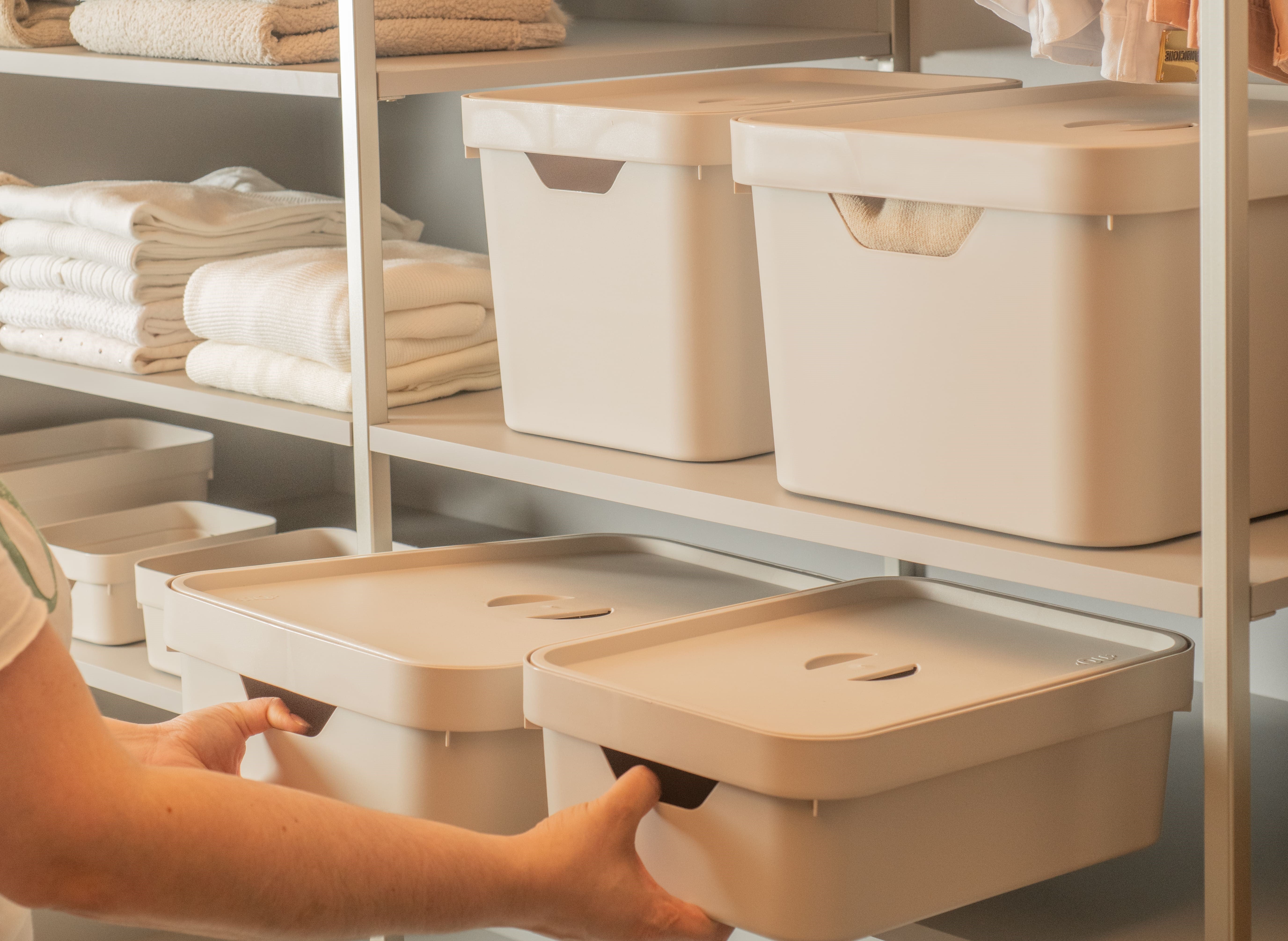 Caixas organizadoras na cor bege sendo colocadas em uma despensa